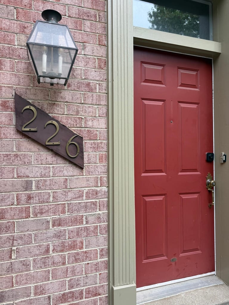 The front door of 226 Lynn Manor Drive, painted red, with brass house numbers on brick